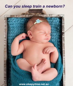 Portrait of a sleeping nine day old newborn baby girl. She is sleeping in a small wooden crate, curled up and swaddled with turquoise blue knit material.